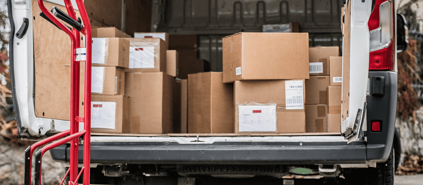 Open delivery van loaded with cardboard boxes, featuring a red dolly cart in the foreground ready for unloading